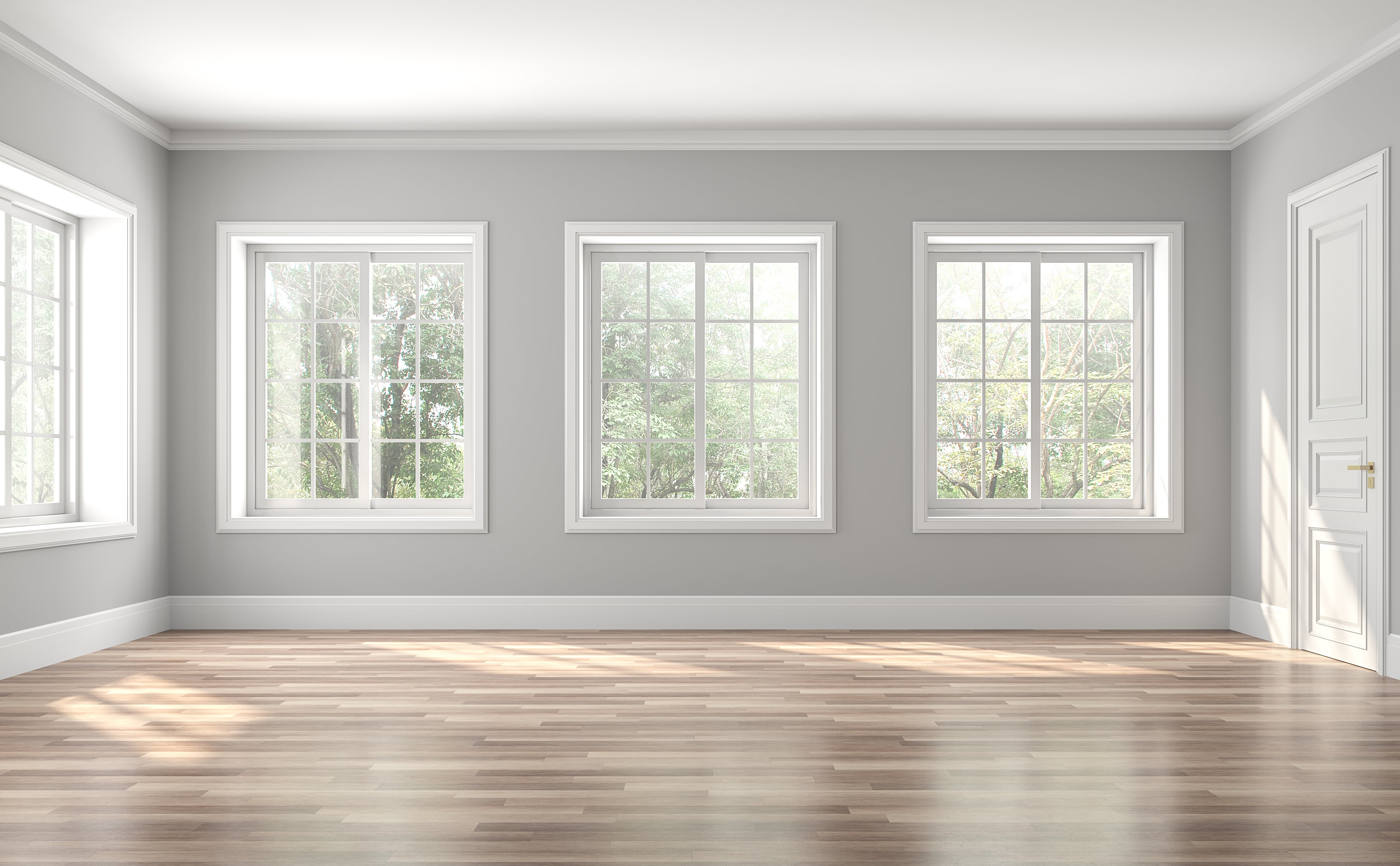 Large empty room with low-gloss light hardwood flooring, pale walls and tall windows