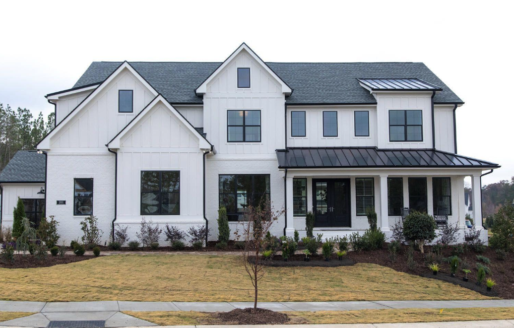 Front view of a modern farmhouse with white siding, black windows, covered porch and clean trim